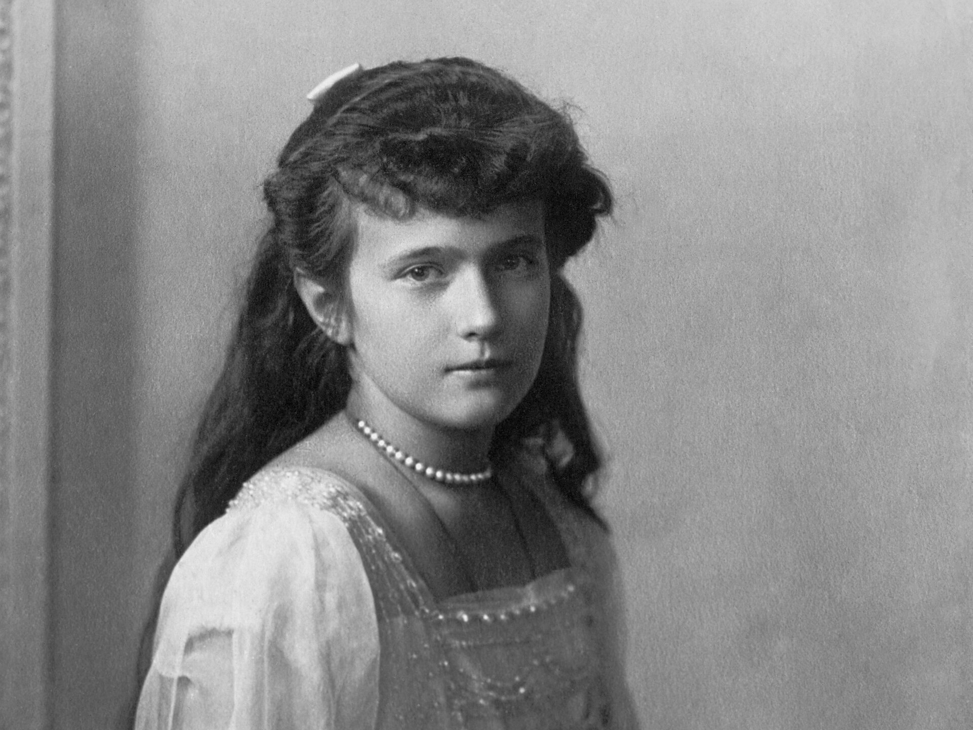 Fotografía antigua en blanco y negro de una adolescente de pelo largo y oscuro, con vestido claro y collar de perlas, sentada
