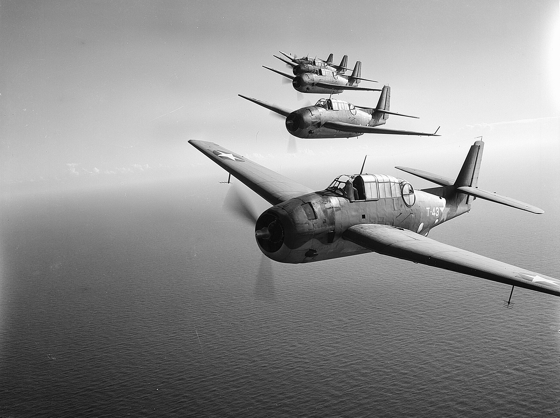 Fotografía en blanco y negro de cuatro aviones militares de un motor volando en fila sobre el mar