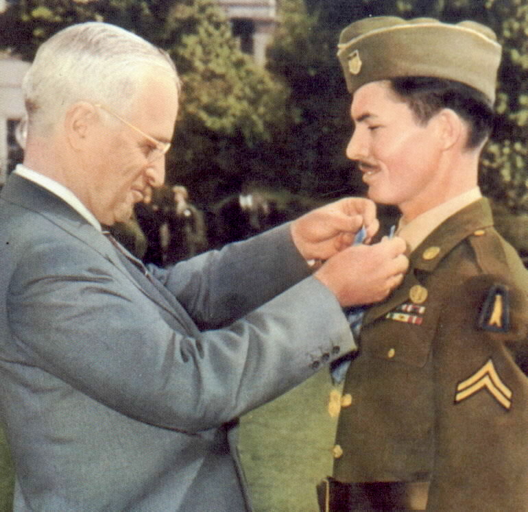 Fotografía en color del presidente Harry Truman colgando una medalla en el cuello de un joven soldado, Desmond Doss
