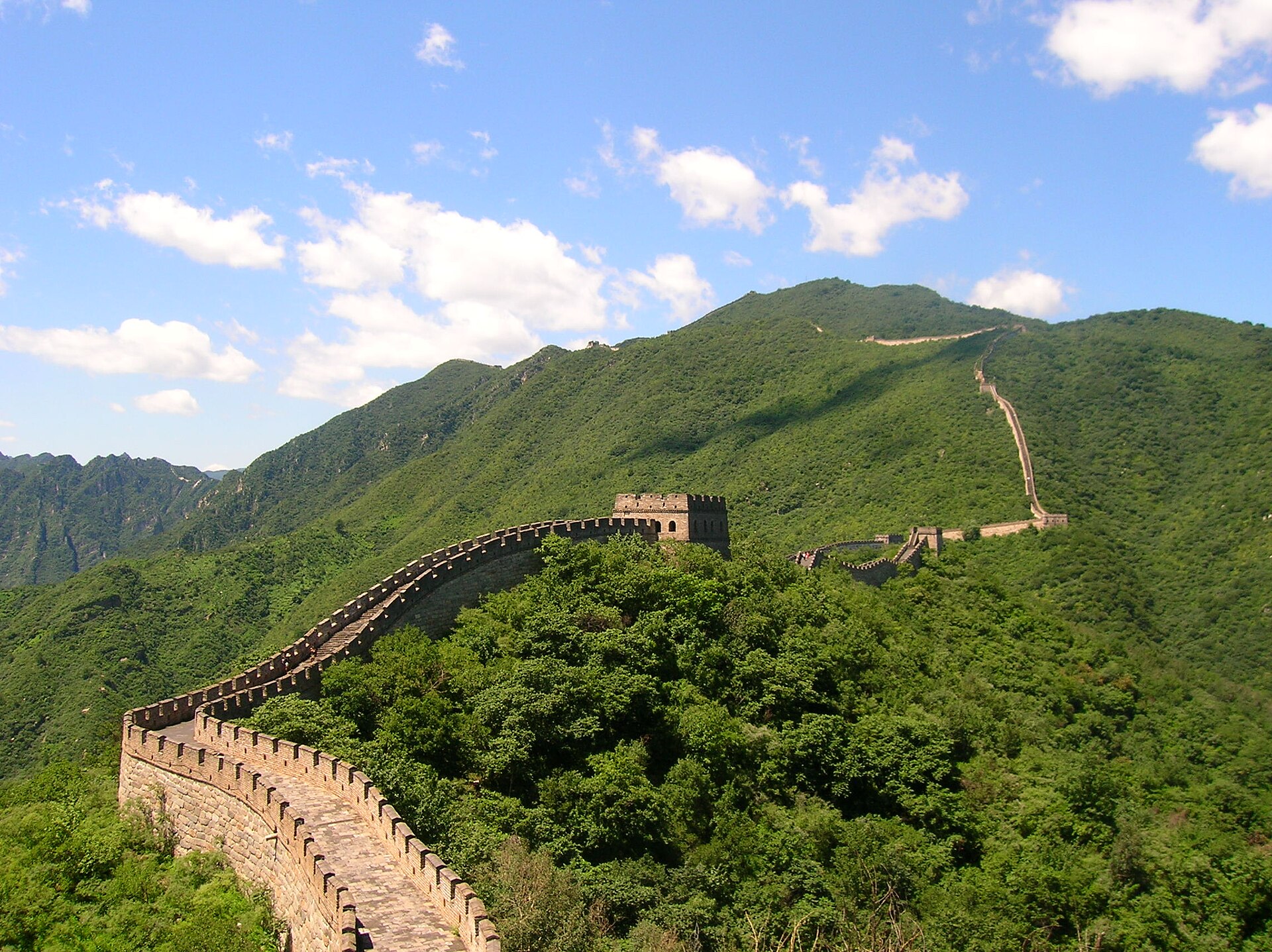 La Gran Muralla China serpenteando por montañas cubiertas de bosque verde bajo un cielo azul