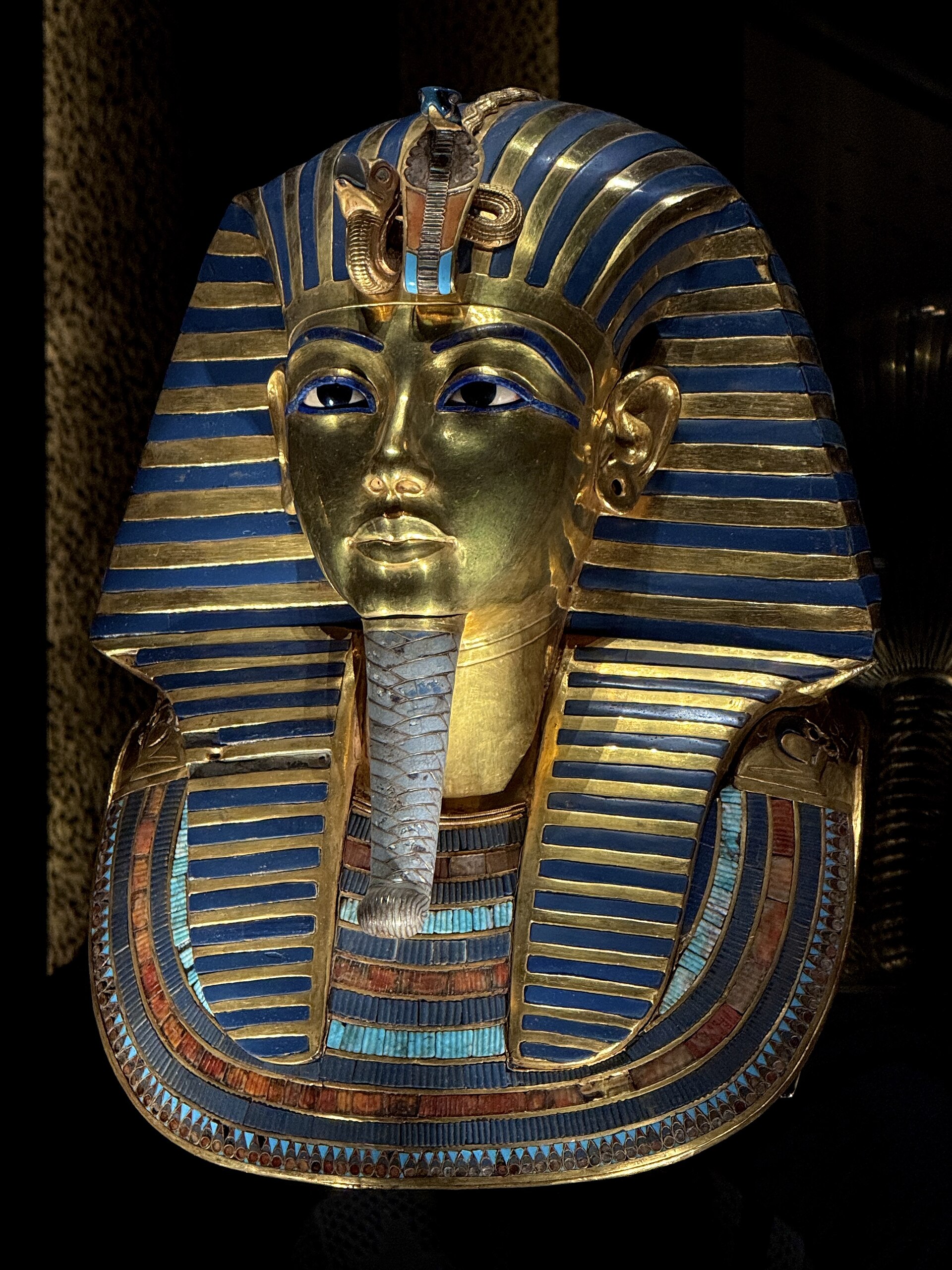 La máscara funeraria de oro de Tutankamón, con franjas azules en el tocado, expuesta en una vitrina
