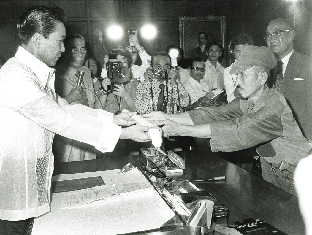 Hiroo Onoda, con gorra y uniforme gastado, entrega su espada al presidente de Filipinas Ferdinand Marcos ante fotógrafos en 1974
