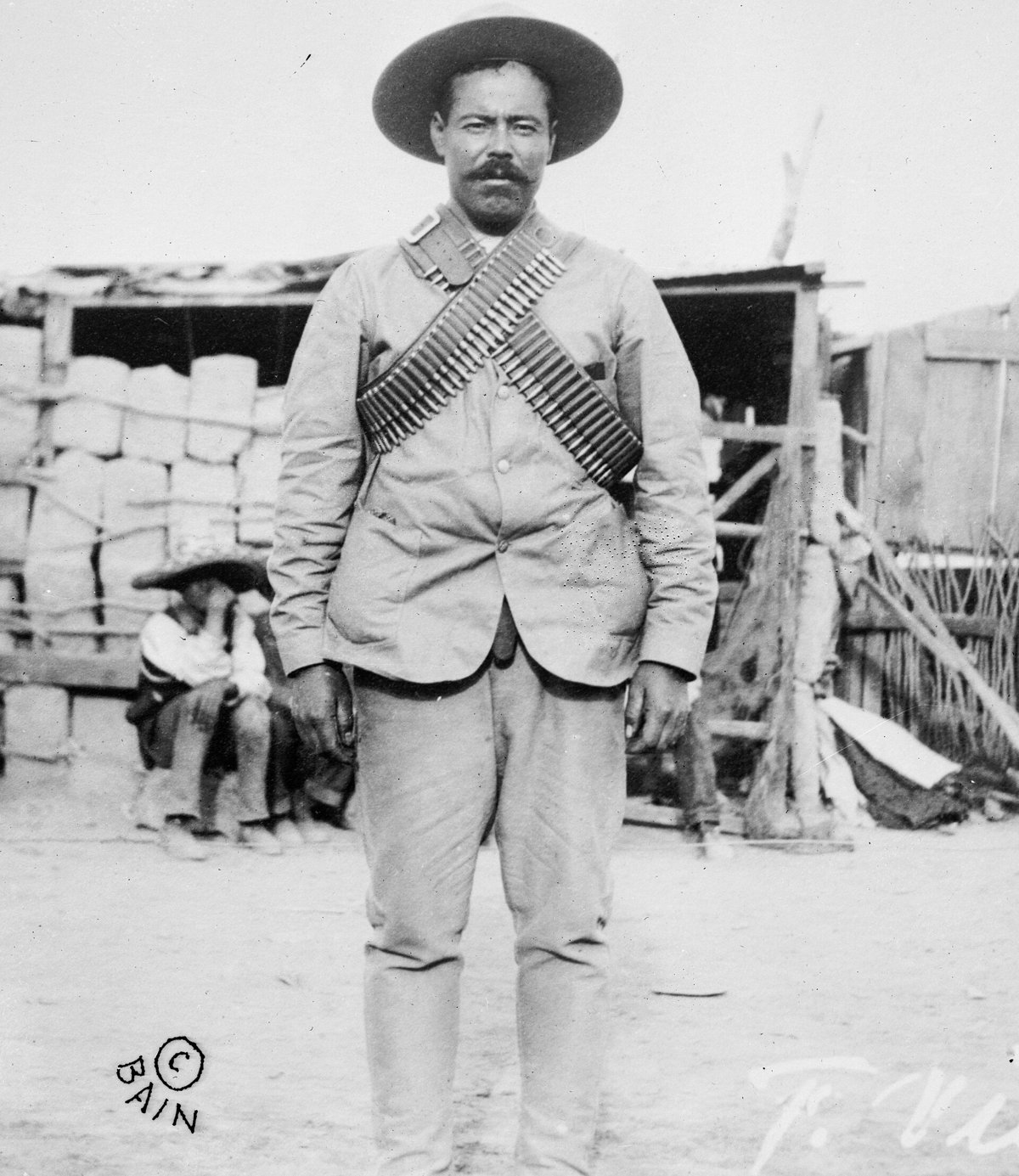 Fotografía antigua en blanco y negro de Pancho Villa de pie, con sombrero de ala ancha y dos cananas de balas cruzadas sobre el pecho